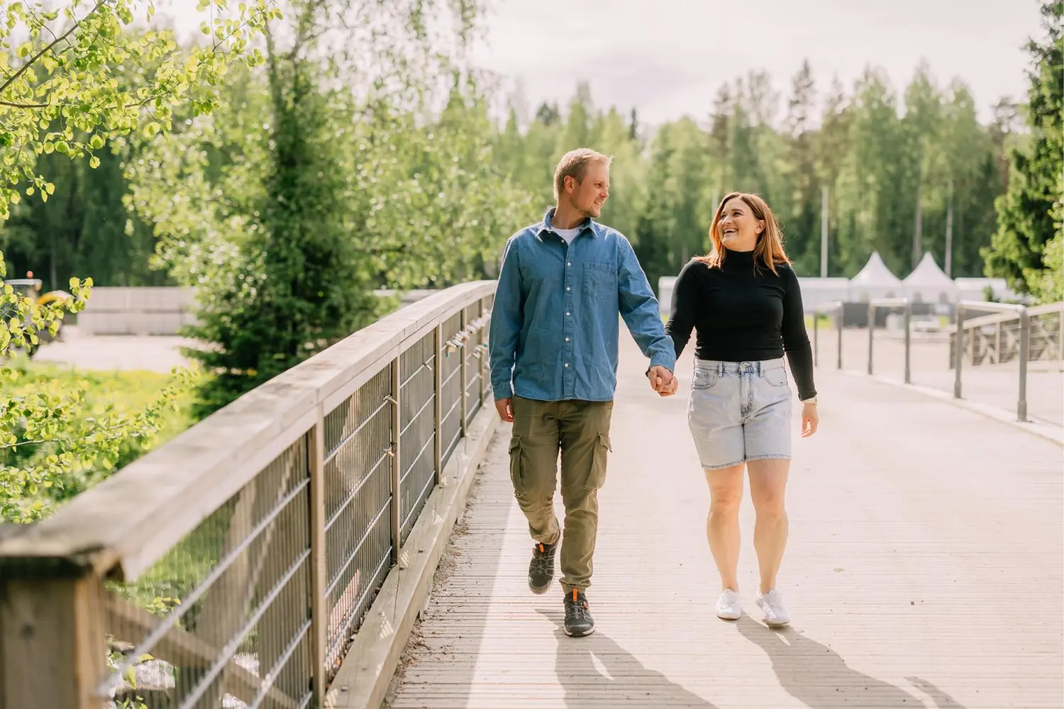 Mies ja nainen kävelevät käsi kädessä puusillalla